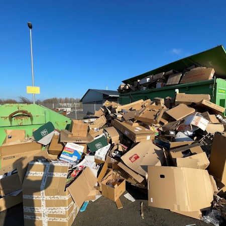 Auf einem Platz in Euskirchen stehen grüne Container. Sie sind mit Altpapier befüllt. Auch davor türmt sich Altpapier, das nicht mehr in die Container passt.