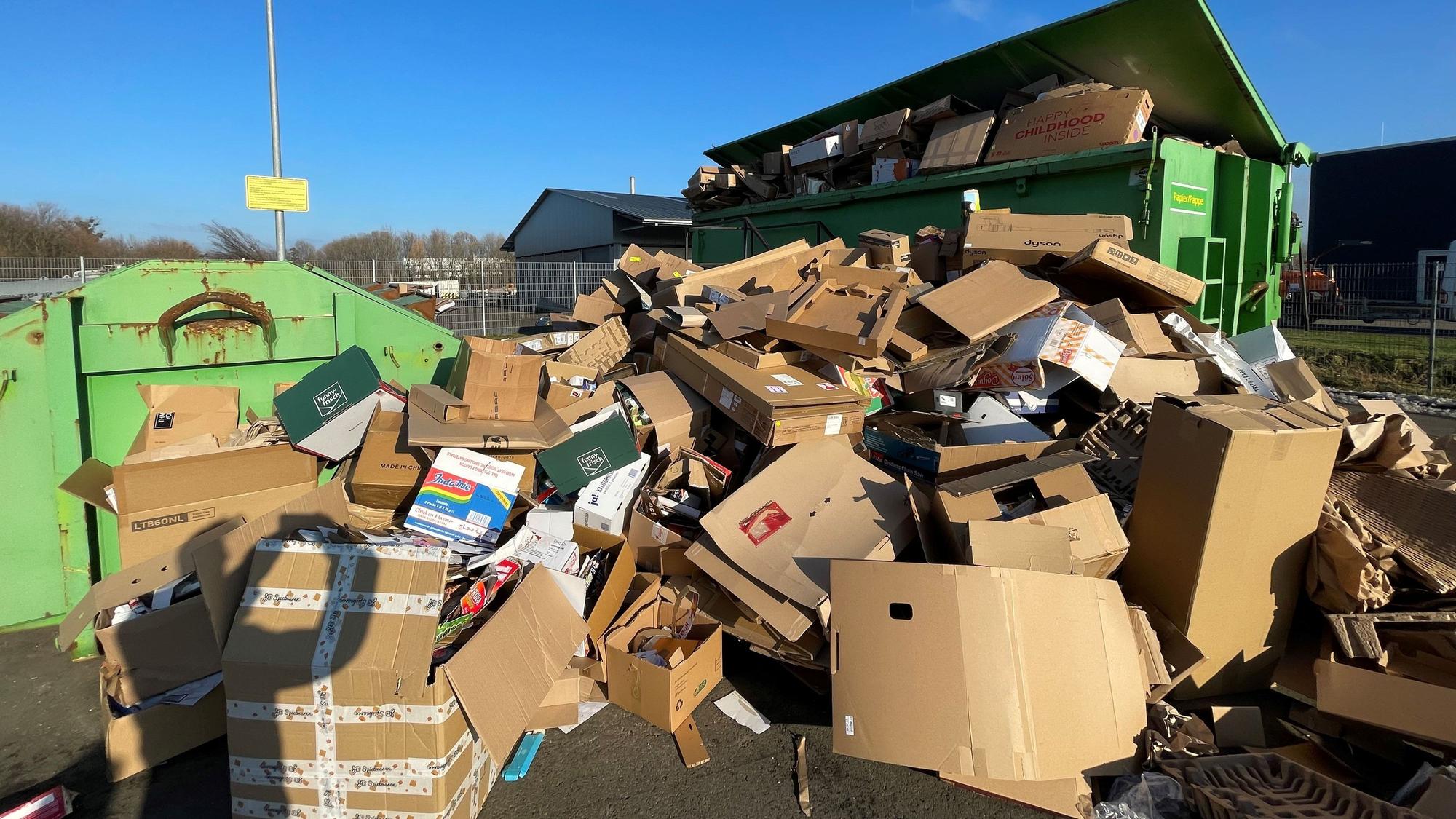 Auf einem Platz in Euskirchen stehen grüne Container. Sie sind mit Altpapier befüllt. Auch davor türmt sich Altpapier, das nicht mehr in die Container passt.