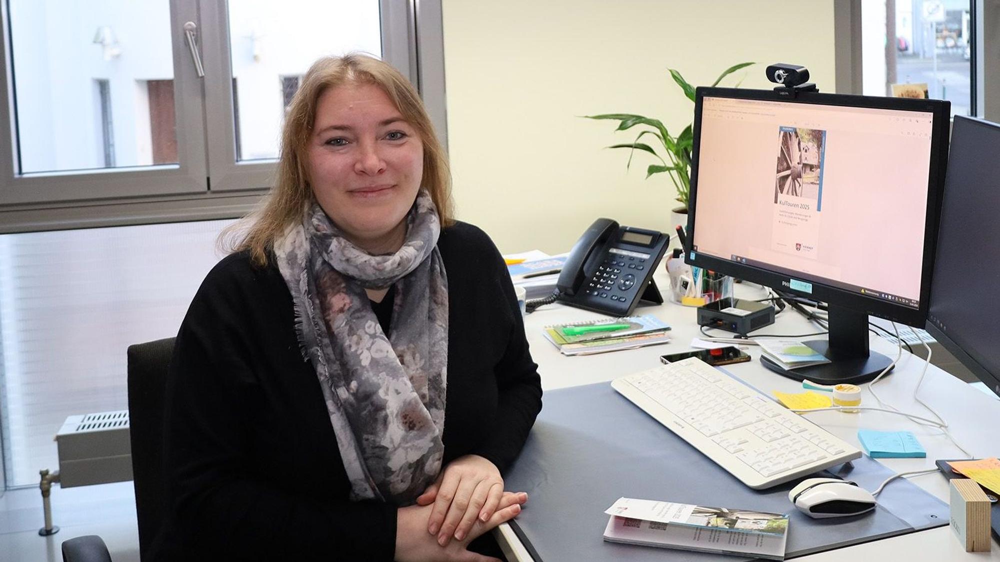 Eine Frau in einem Büro mit Schreibtisch und Computer-Monitor.