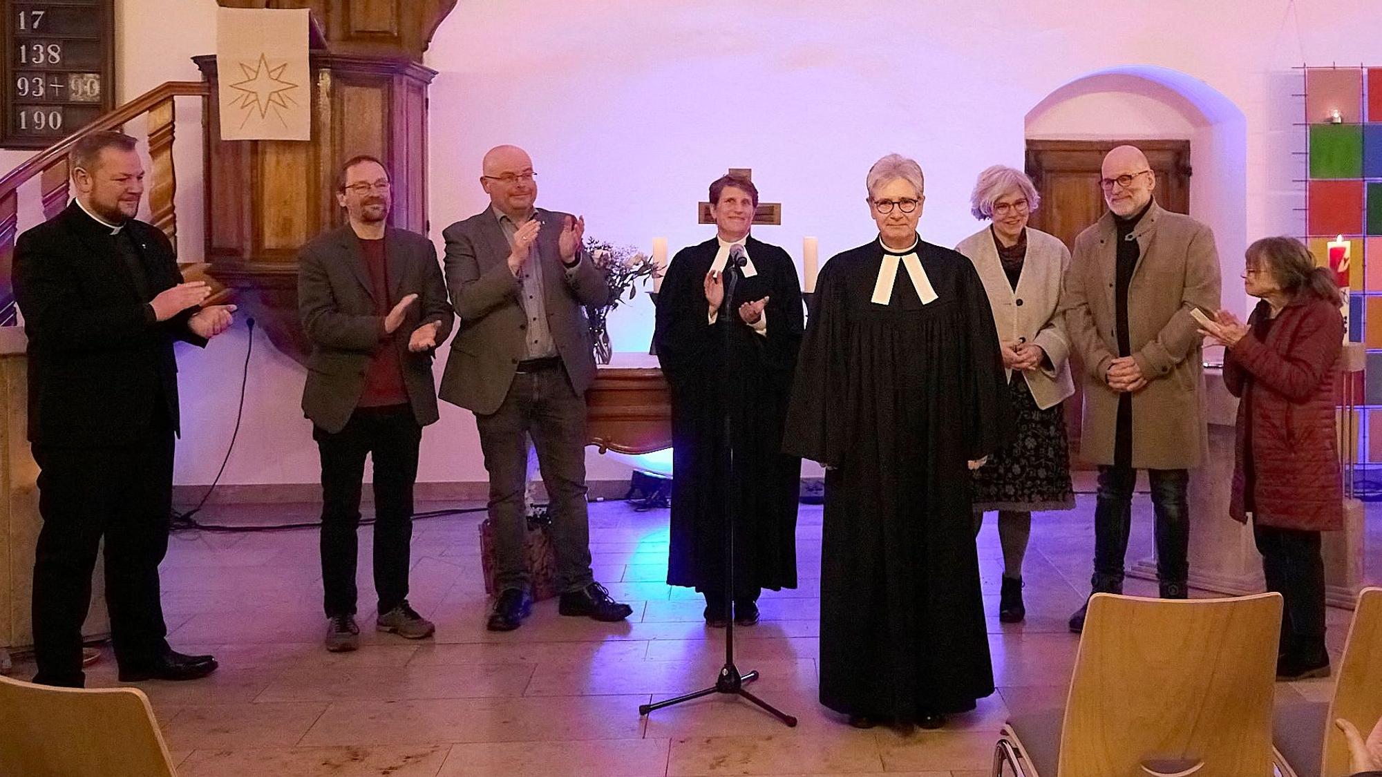 Die Pfarrerin ist vorgetreten, während ihre Amtskollegen und Vertreter der beiden evangelischen Kirchengemeinden im Hintergrund applaudieren.