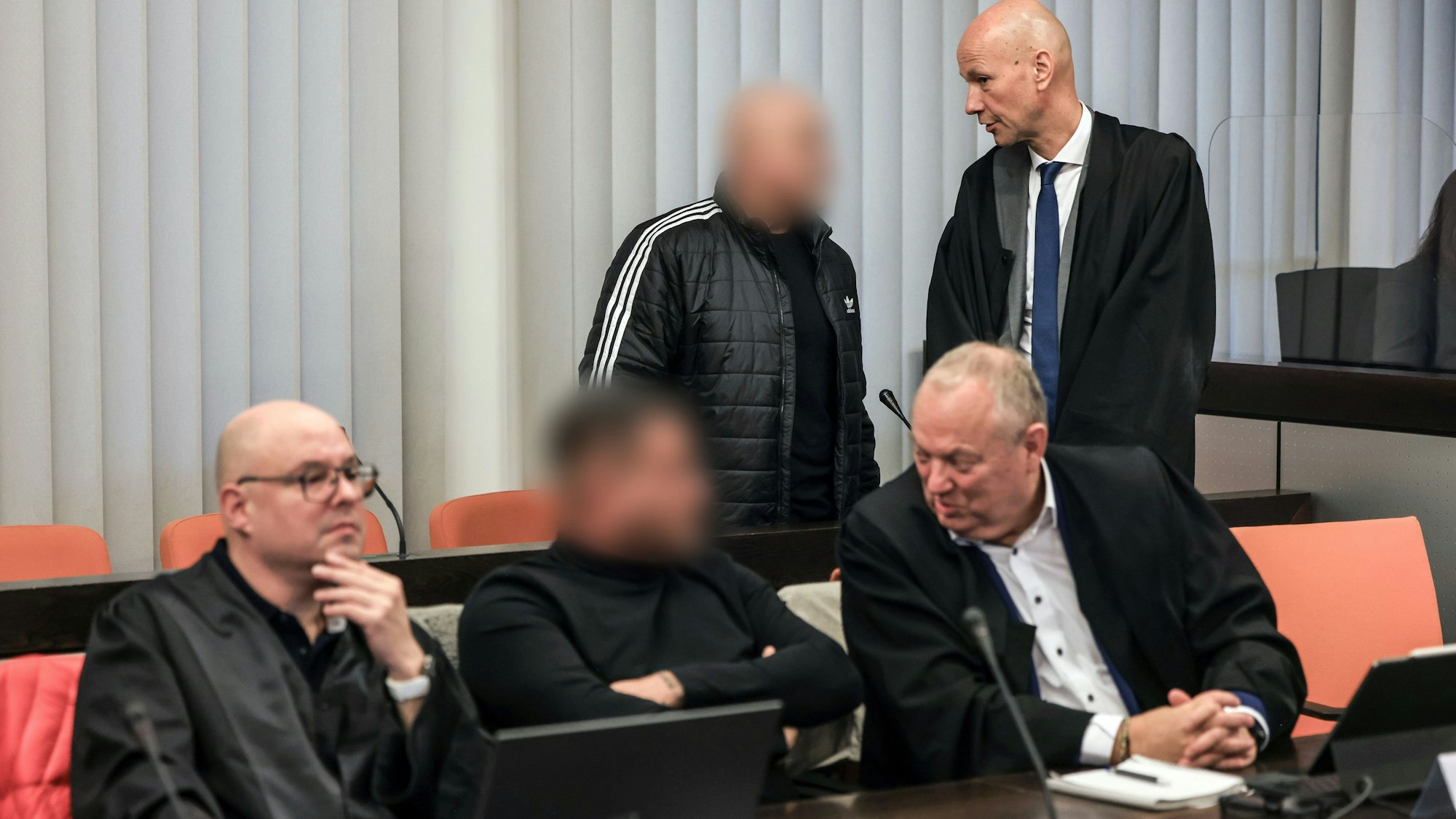 Eine Szene aus dem Gericht: Der Hauptangeklagte spricht im Gerichtssaal mit seinem Verteidiger, während vorne ein Angeklagter mit seinem Verteidiger Hartmut Moyzio spricht. Die Tatverdächtigen sind verpixelt.