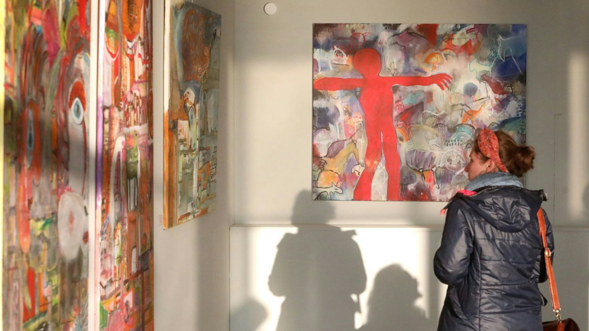 Eine Frau betrachtet großformatige Bilder, die sehr bunt sind.