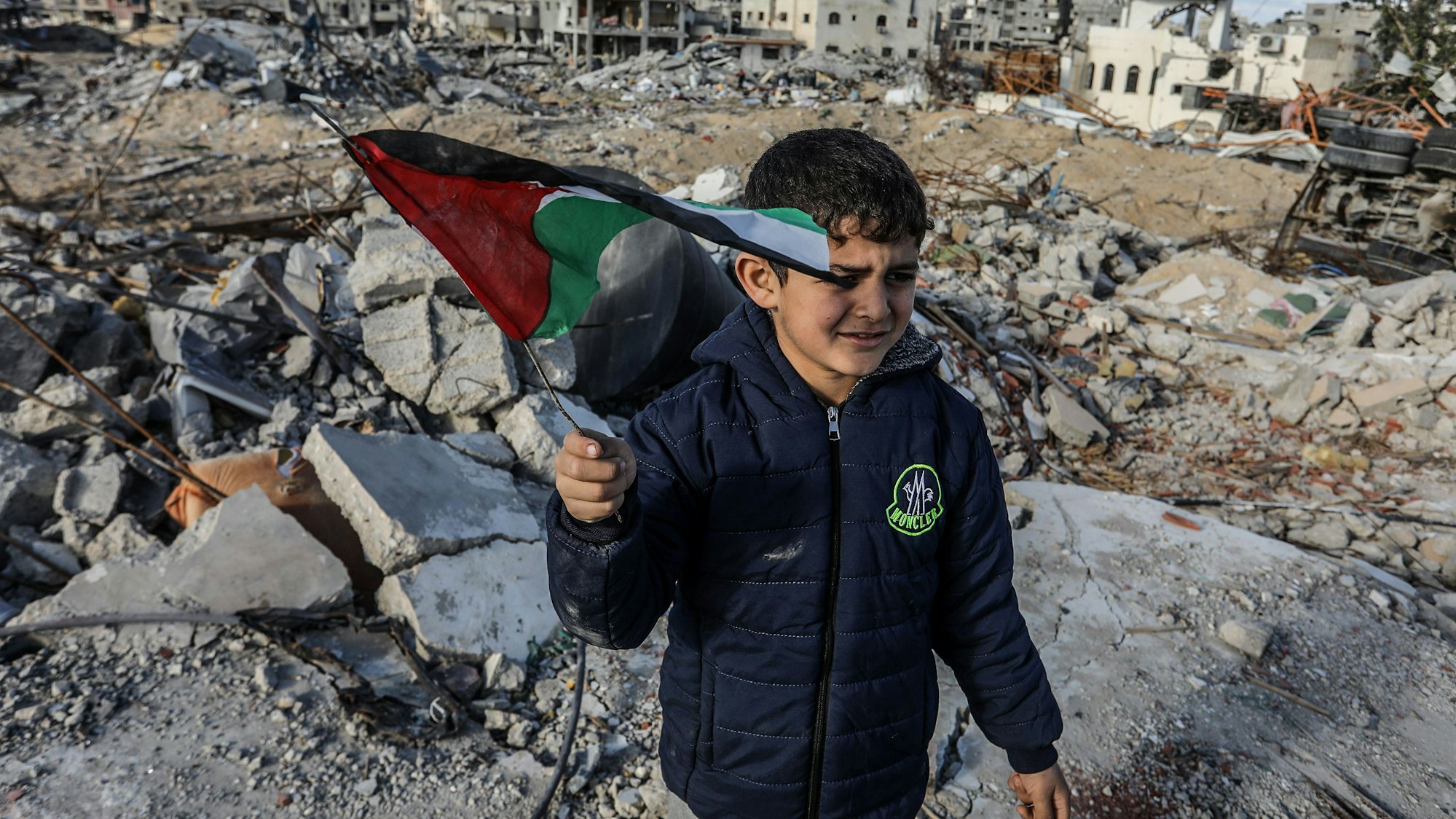 Ein vertriebener palästinensischer Junge, der eine Fahne schwenkt, steht auf Trümmern von Gebäuden, einen Tag nach Inkrafttreten eines Abkommens über eine Waffenruhe zwischen Israel und der Hamas im Gazastreifen.