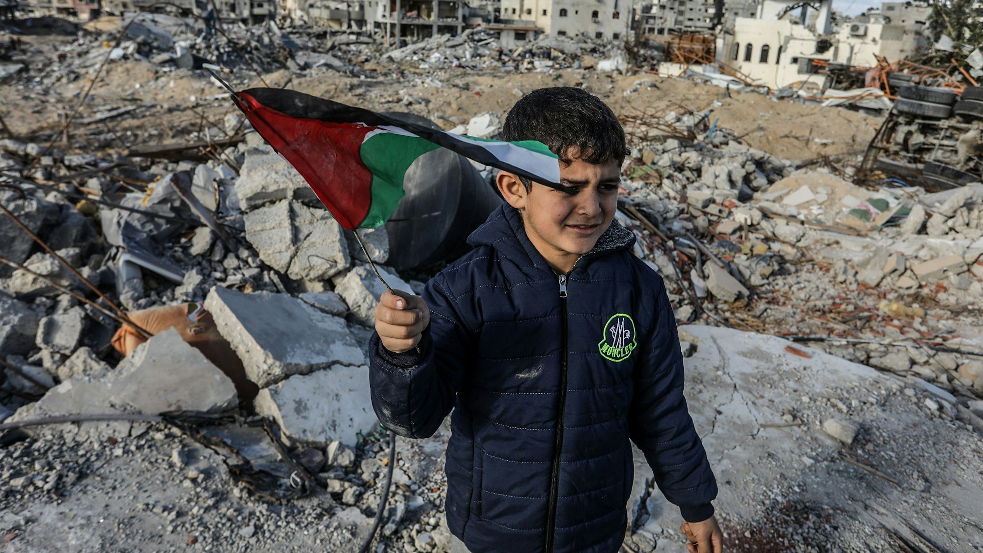 Ein vertriebener palästinensischer Junge, der eine Fahne schwenkt, steht auf Trümmern von Gebäuden, einen Tag nach Inkrafttreten eines Abkommens über eine Waffenruhe zwischen Israel und der Hamas im Gazastreifen.