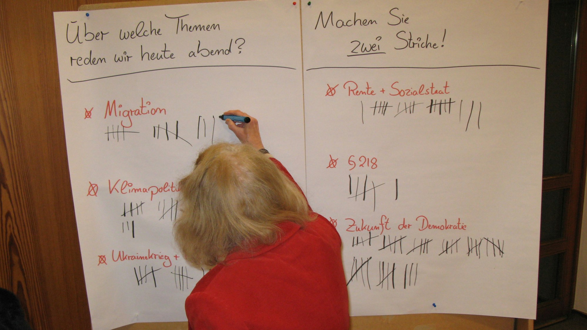 Eine Frau macht mit einem Filzstift einen Strich auf einem Plakat mit Gesprächsthemen-Vorschlägen.