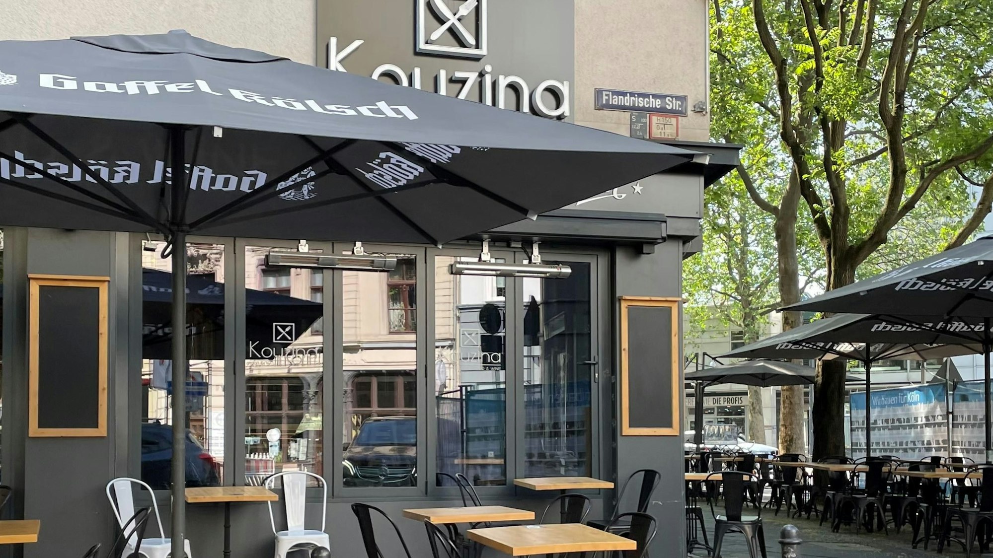 Kouzina in Köln von außen mit Schirmen, Tischen und Stühlen.