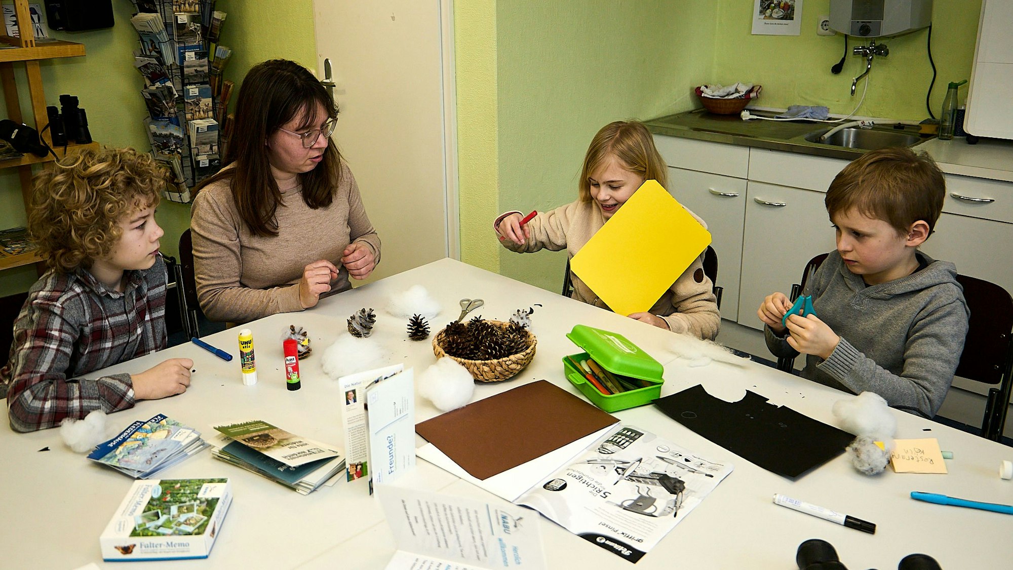 Drei Kinder und eine erwachsene Betreuerin sitzen an einem Tisch und basteln.