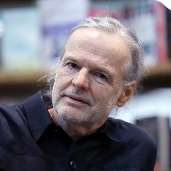 Wolf Haas sitz vor einem Bücherregal.