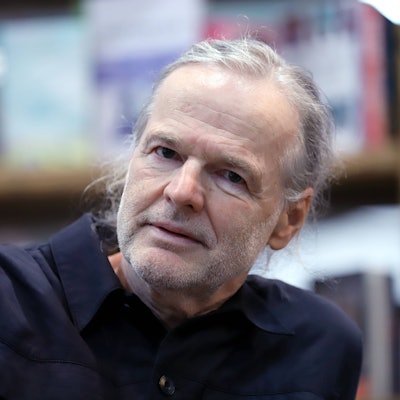 Wolf Haas sitz vor einem Bücherregal.