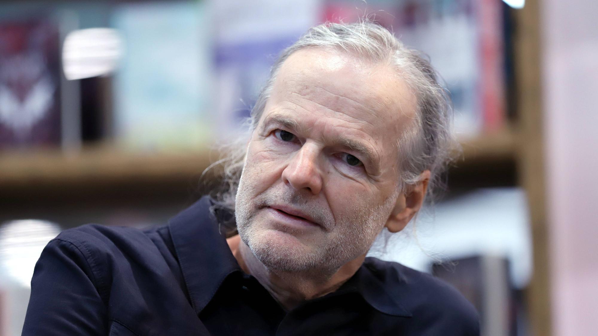 Wolf Haas sitz vor einem Bücherregal.