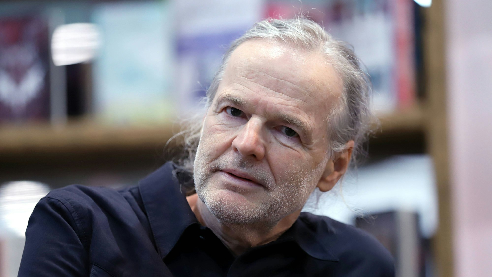 Wolf Haas sitz vor einem Bücherregal.