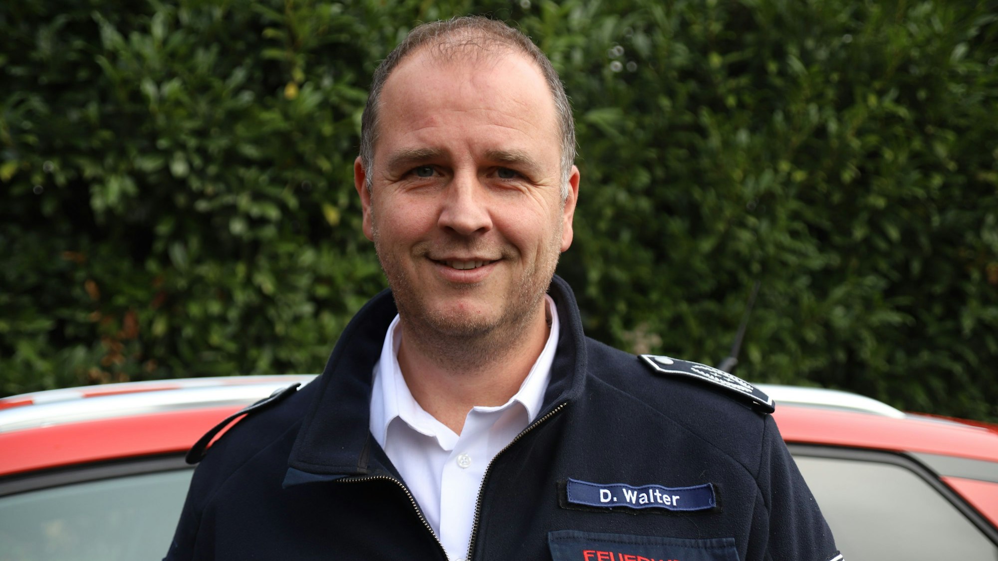 Ein Feuerwehrmann steht vor einem roten Auto.