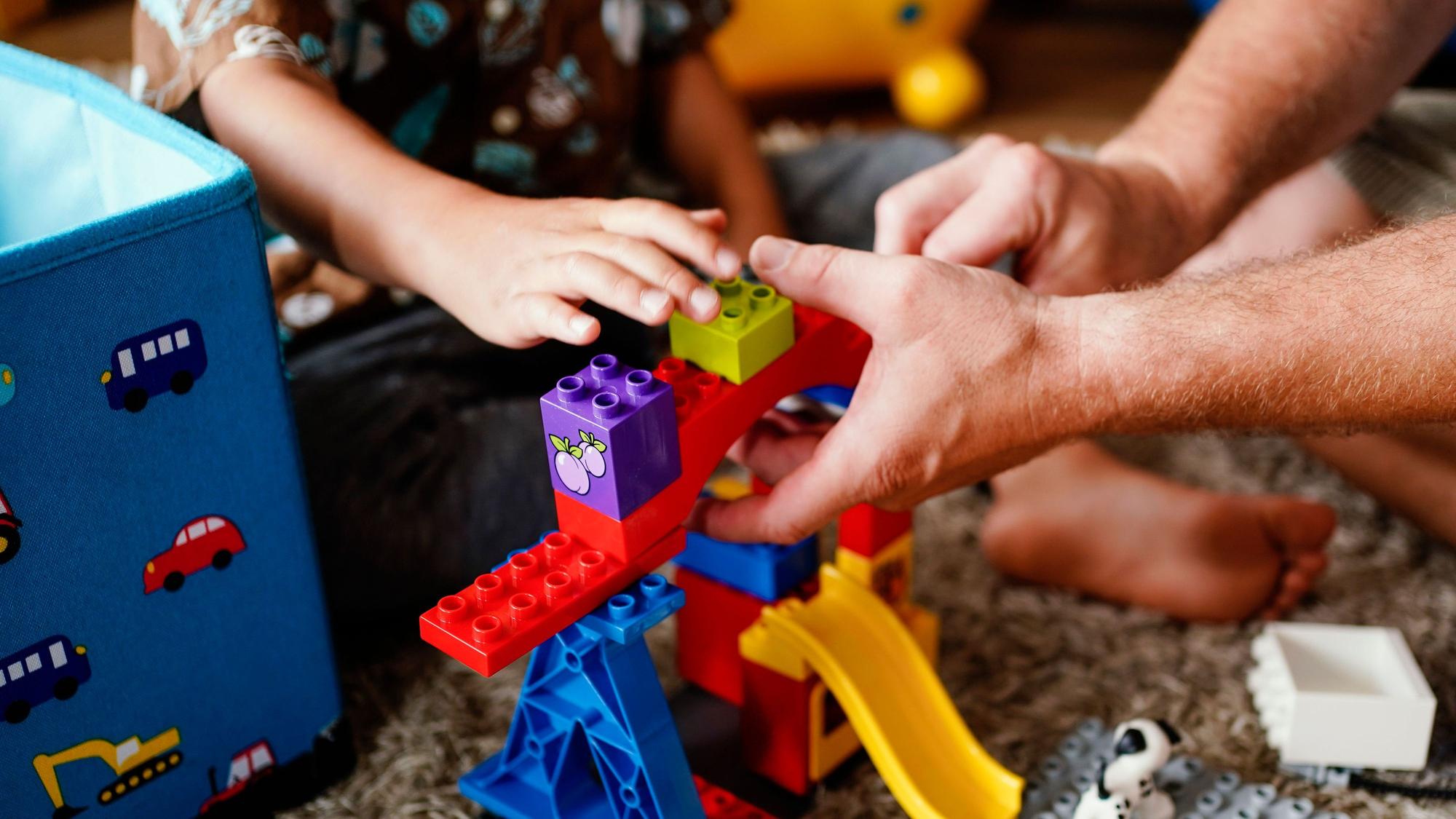 ARCHIV - 24.06.2021, Baden-Württemberg, Heidelberg: Ein Pflegevater spielt mit einem Pflegekind im Wohnzimmer. Tausende Kinder wachsen in Pflegefamilien auf. (zu dpa: «Mangel an Pflegefamilien und Personal in Jugendhilfe in NRW») Foto: Uwe Anspach/dpa - ACHTUNG: Dieses Foto hat dpa bereits im Bildfunk gesendet +++ dpa-Bildfunk +++