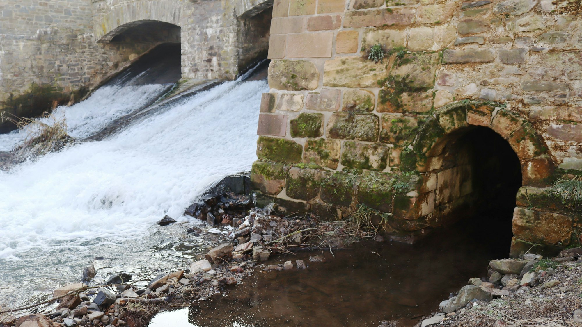 Ein Stolleneingang befindet sich unterhalb der Stadtmauer. Im Hintergrund fließt die Erft über die Wasserfälle in die Stadt.