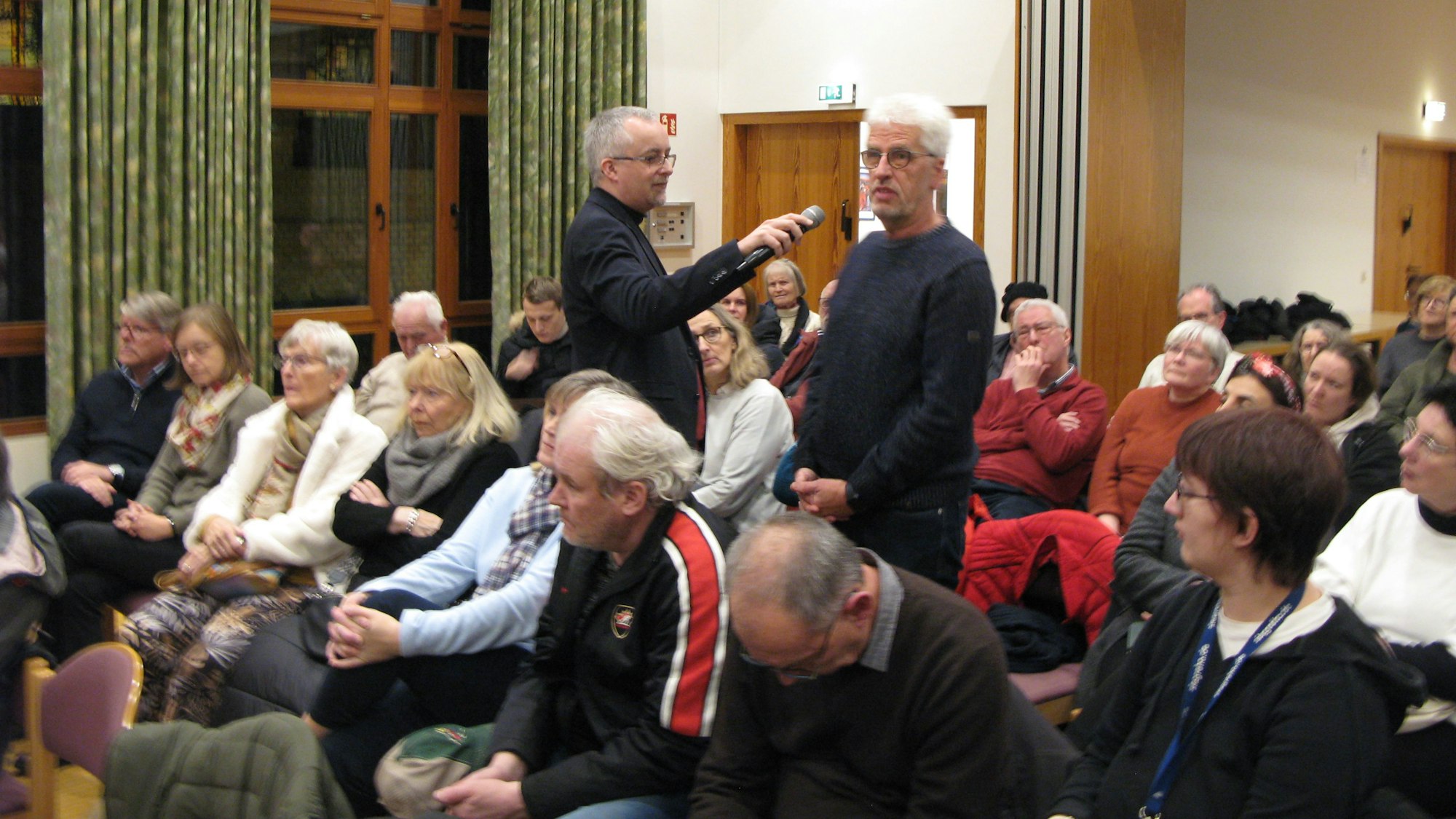 Ein Saal mit gefüllten Stuhlreihen, ein Mann spricht in ein Mikrofon.