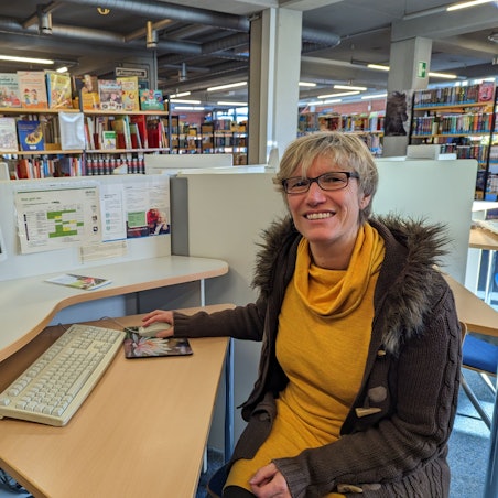 Das Foto zeigt die Büchereileiterin an einem Computerarbeitsplatz, im Hintergrund die alten Bücherregale.