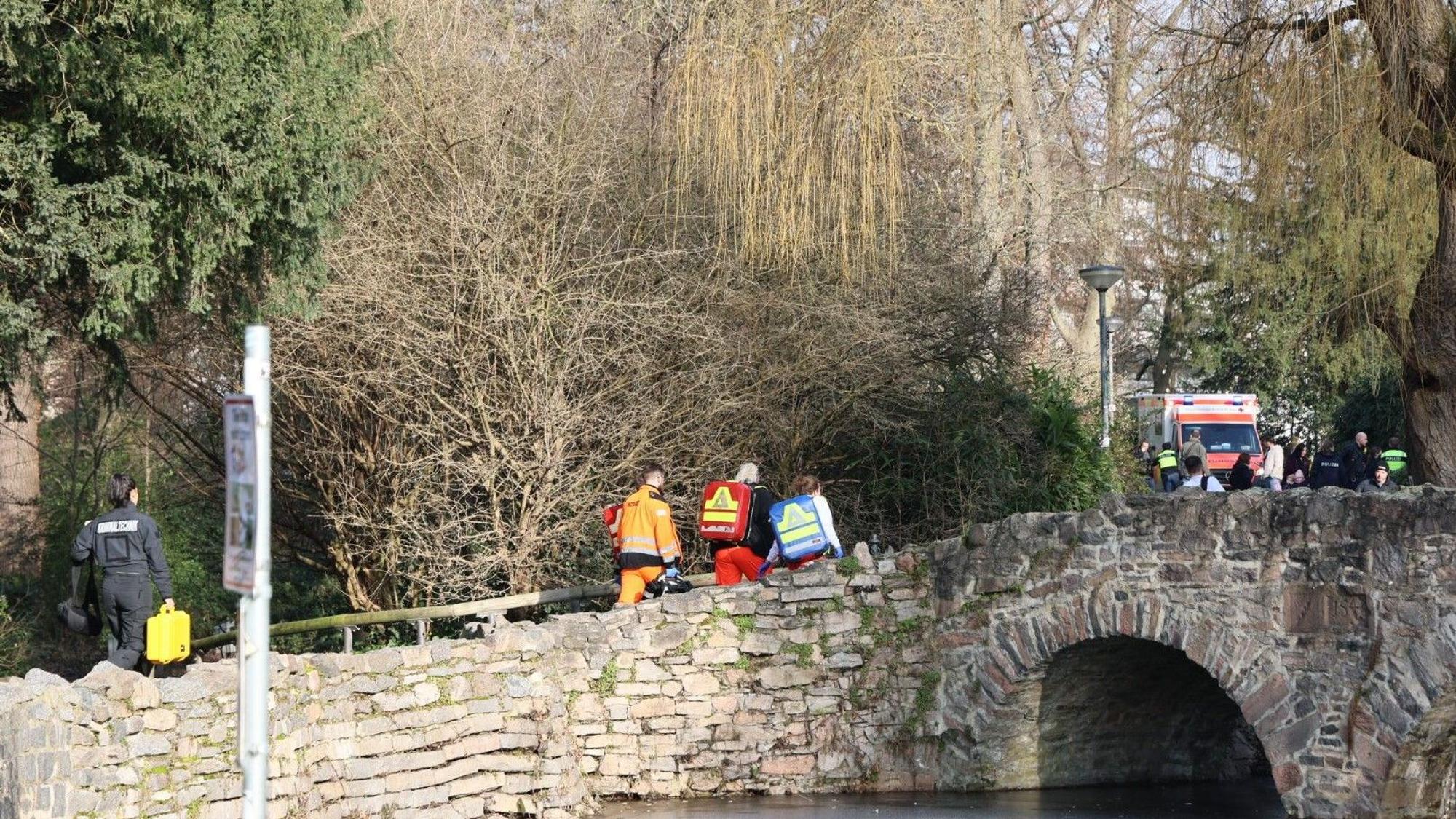Rettungskräfte und Kriminaltechniker gehen in der Nähe eines Tatortes in Aschaffenburg eine kleine Brücke hinauf.
