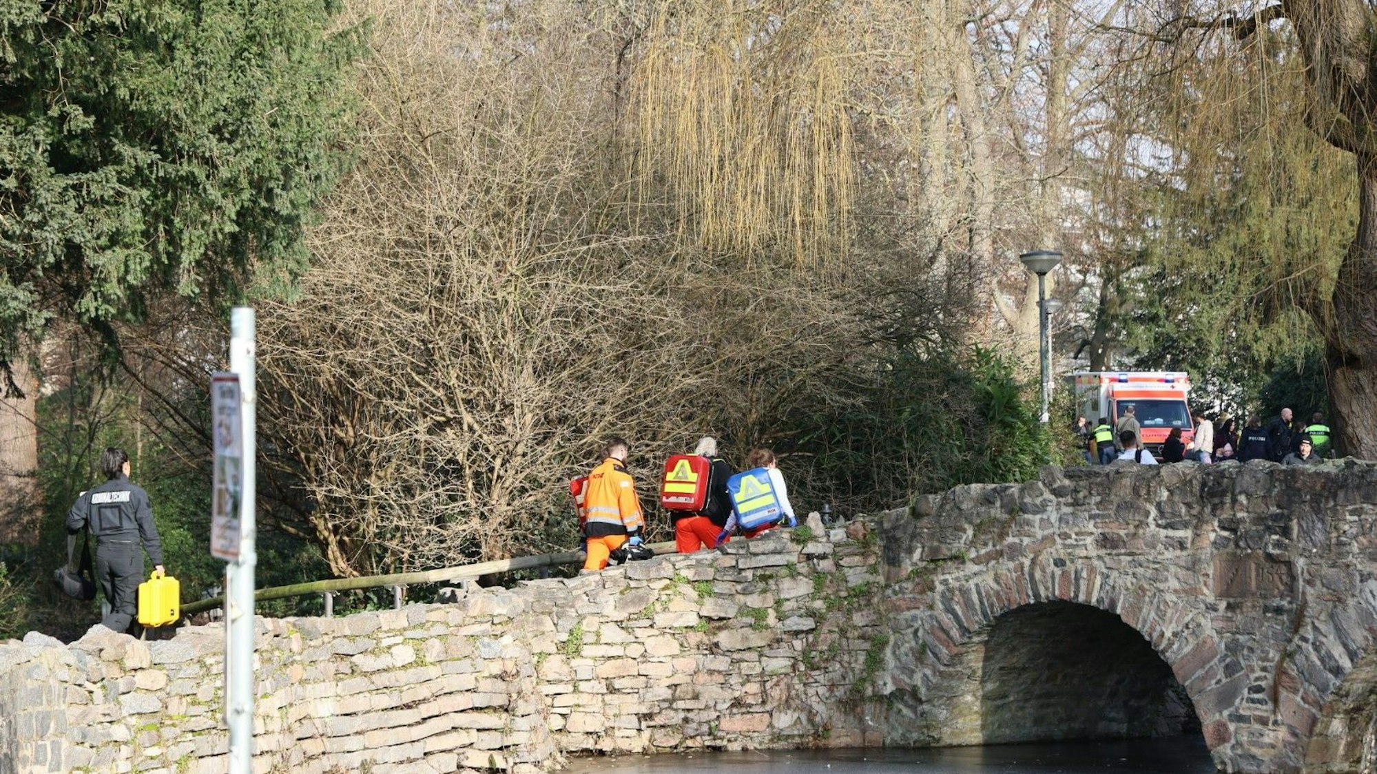 Rettungskräfte und Kriminaltechniker gehen in der Nähe eines Tatortes in Aschaffenburg eine kleine Brücke hinauf.