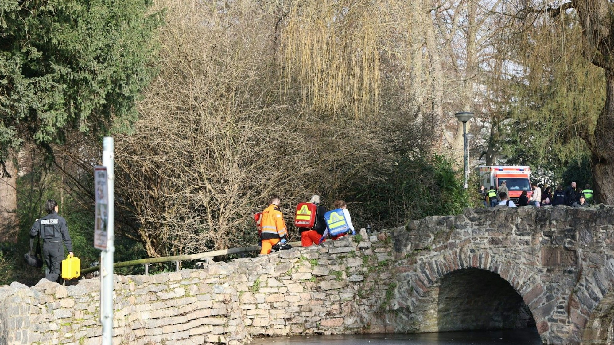 Rettungskräfte und Kriminaltechniker gehen in der Nähe eines Tatortes in Aschaffenburg eine kleine Brücke hinauf.