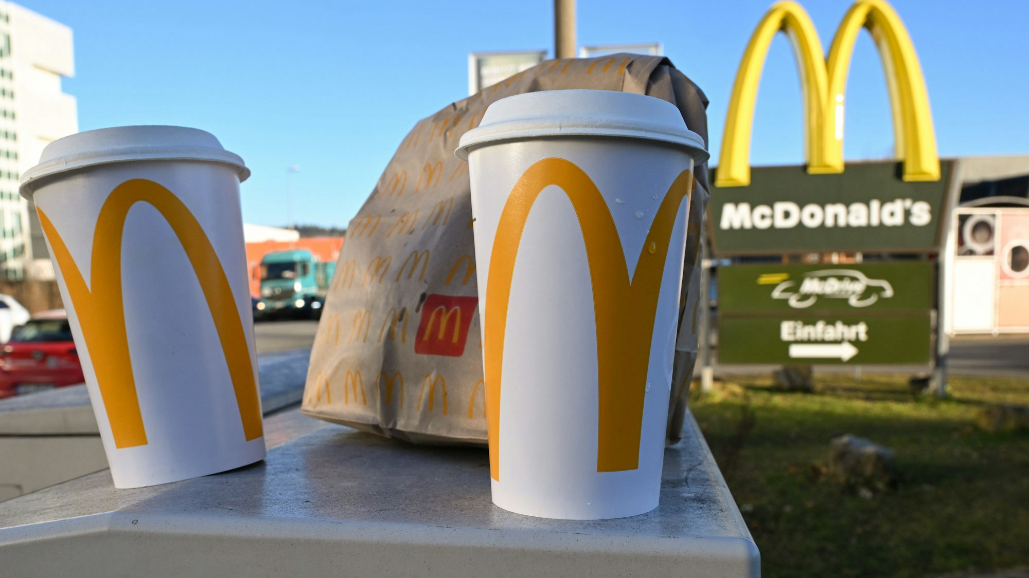 Eine McDonald's To-Go-Tüte und ein To-Go-Becher stehen vor einer Tübinger McDonald's-Filiale.