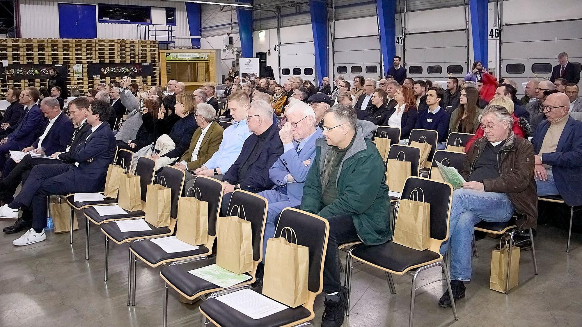 Zahlreiche Menschen sitzen auf Stühlen in einer Halle im Logistikzentrum von Papstar in Kall.