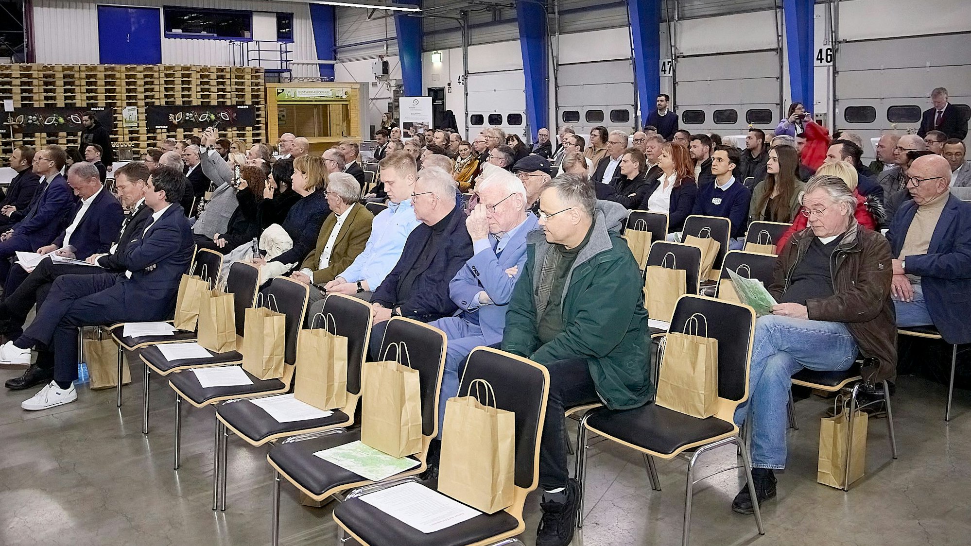Zahlreiche Menschen sitzen auf Stühlen in einer Halle im Logistikzentrum von Papstar in Kall.
