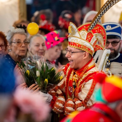 Karnevalsprinz Jens Pesch verteilt in einem Saal voller Senioren Tulpensträuße.