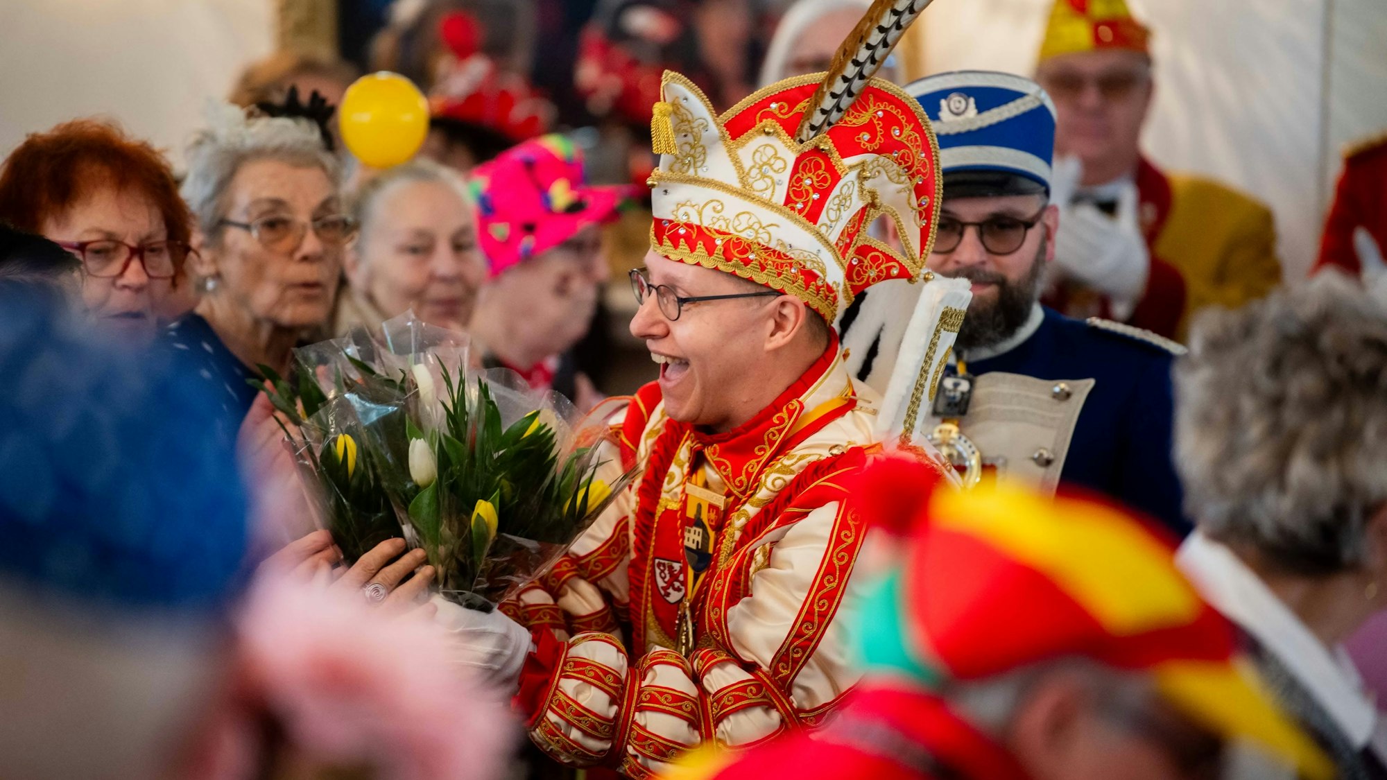 Karnevalsprinz Jens Pesch verteilt in einem Saal voller Senioren Tulpensträuße.