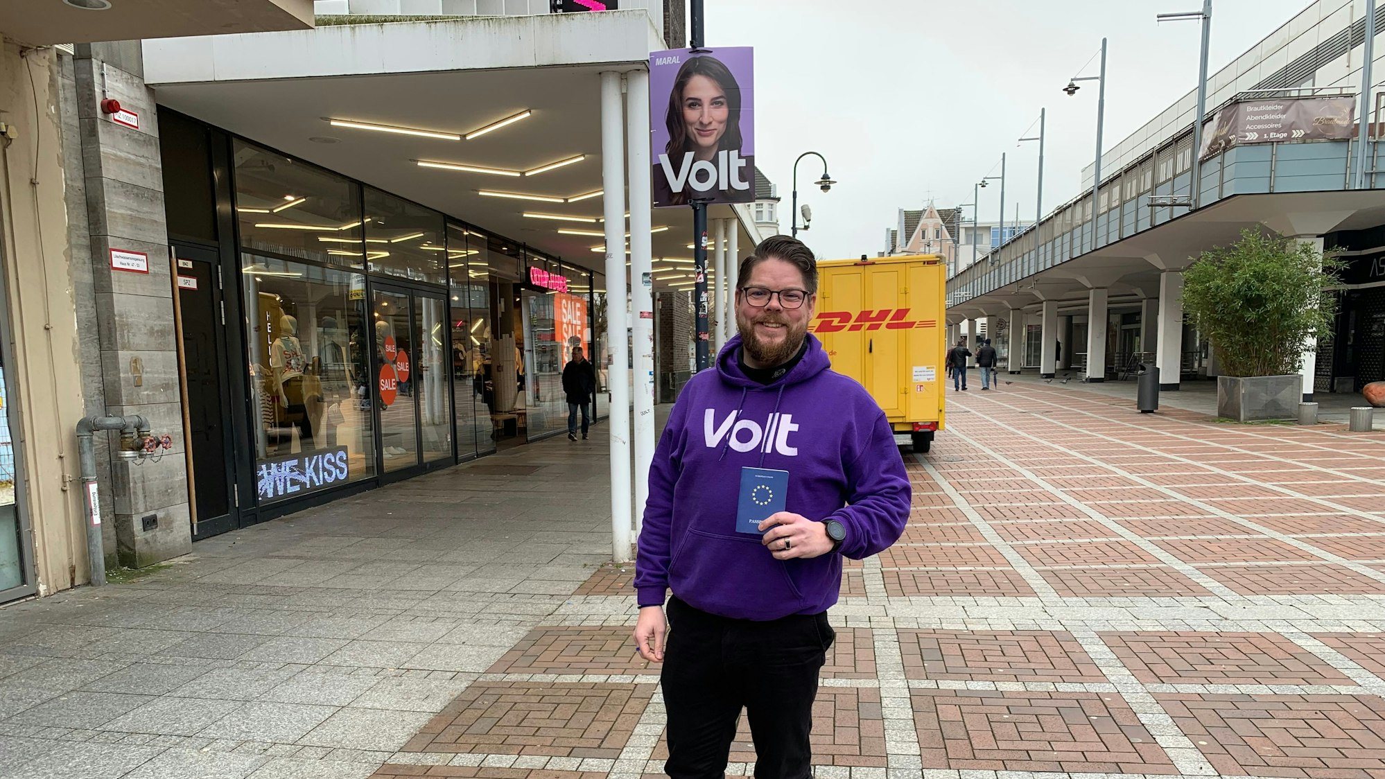 Ein Mann steht in einer Fußgängerzone und hält einen Pass in den Händen.