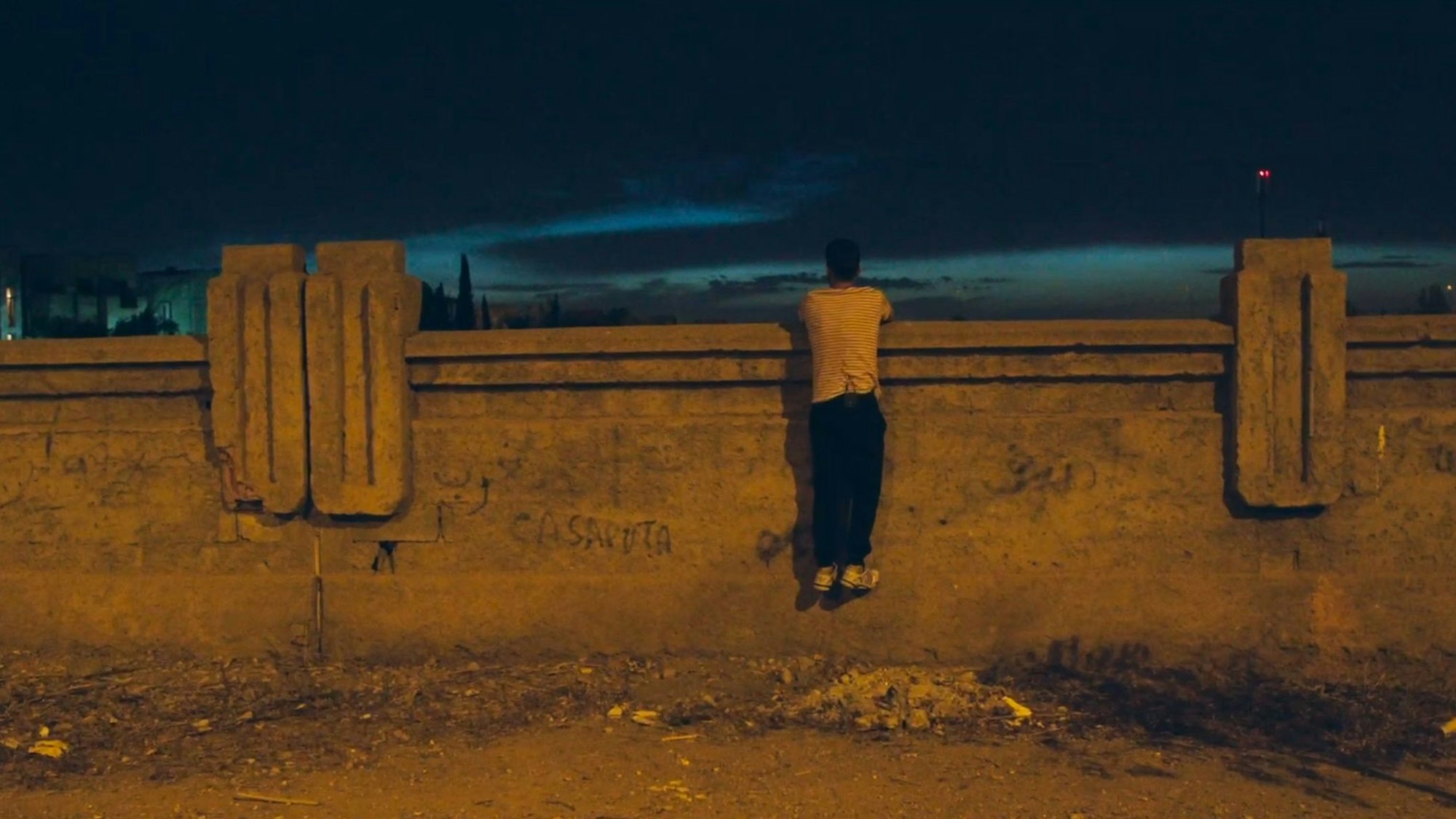 Ein Mann hängt an einer Wand und schaut über diese hinweg in die Nacht.