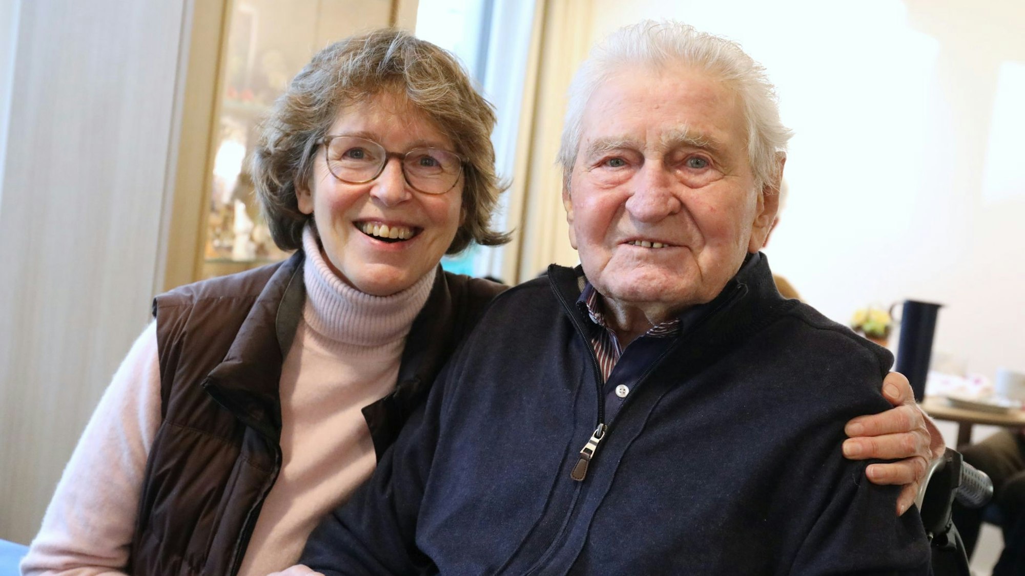 Eine Frau und ein Mann sitzen nebeneinander, sie hat einen Arm um ihn gelegt.