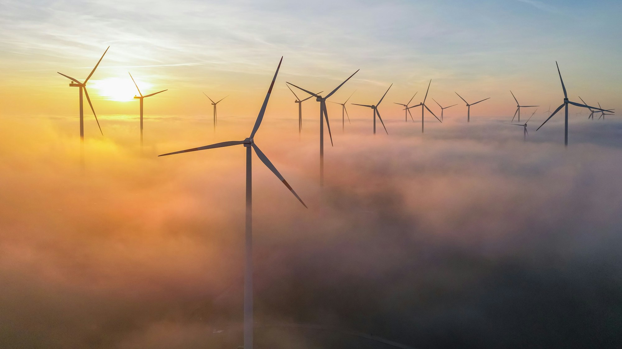 Die Morgensonne leuchtet über dem Nebel zwischen Windenergieanlagen im östlichen Brandenburg (Luftaufnahme mit einer Drohne).