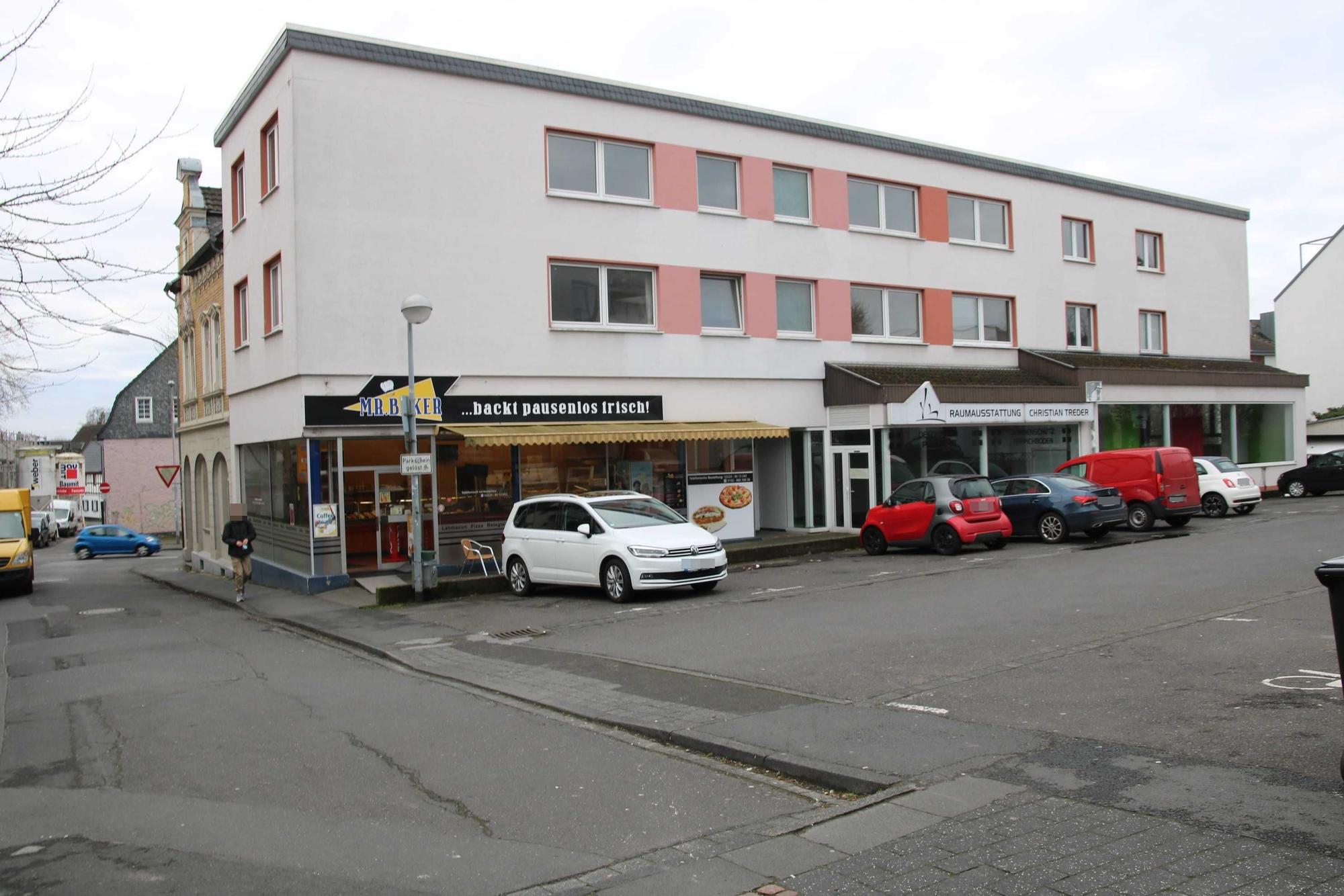 Ein dreigeschossiges Gebäude mit einem Parkplatz davor.