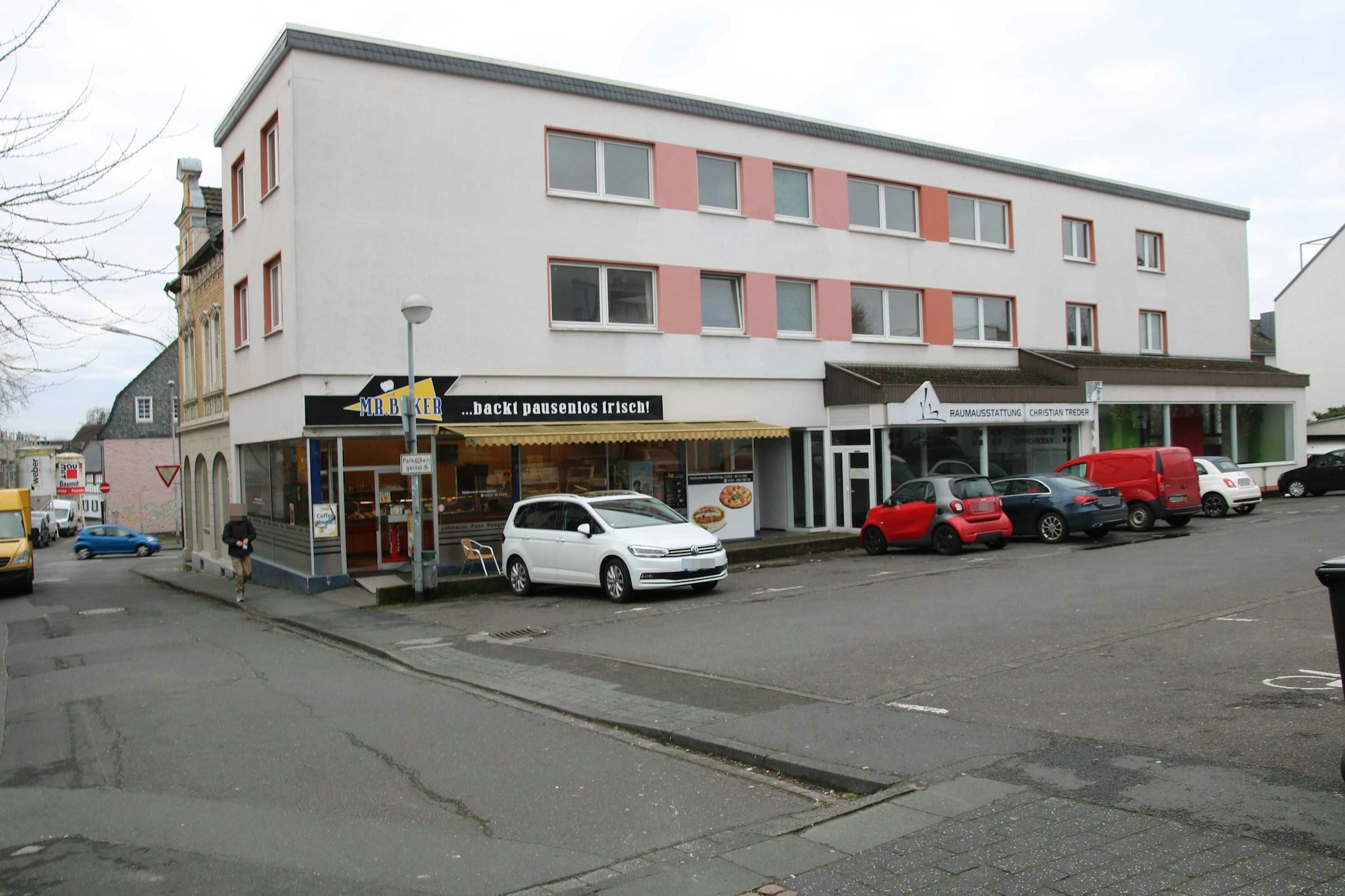 Ein dreigeschossiges Gebäude mit einem Parkplatz davor.