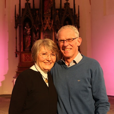 Ein Mann und eine Frau stehen vor einer rosa beleuchteten Wand und lächeln.