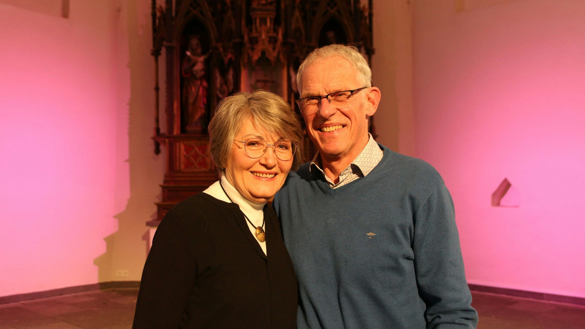 Ein Mann und eine Frau stehen vor einer rosa beleuchteten Wand und lächeln.