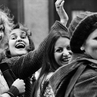 Vier Frauen winken lachend in die Kamera.