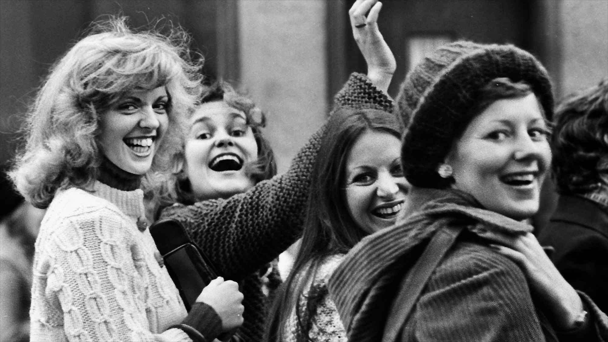 Vier Frauen winken lachend in die Kamera.
