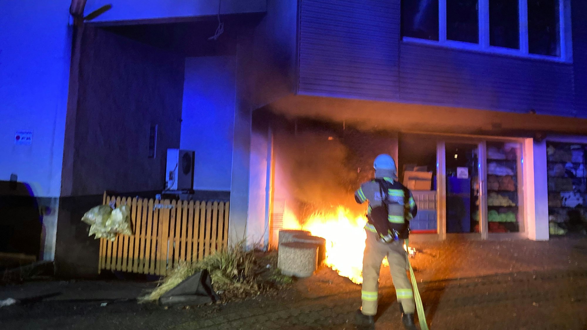 Ein Feuerwehrmann löscht Flammen an einem Wohn- und Geschäftshaus in Bergisch Gladbach.