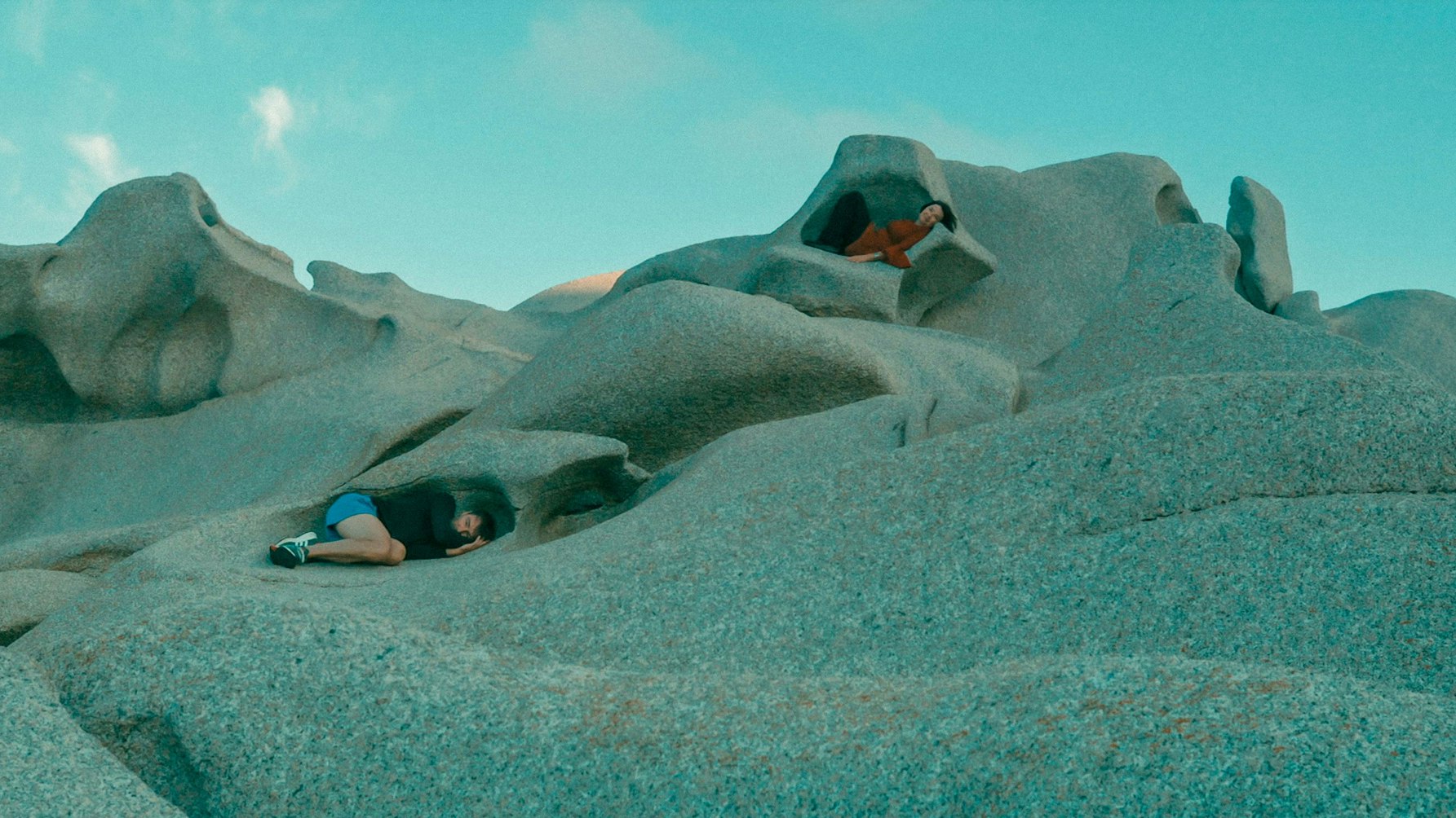 Zwei Menschen liegen in Mulden einer Berglandschaft.