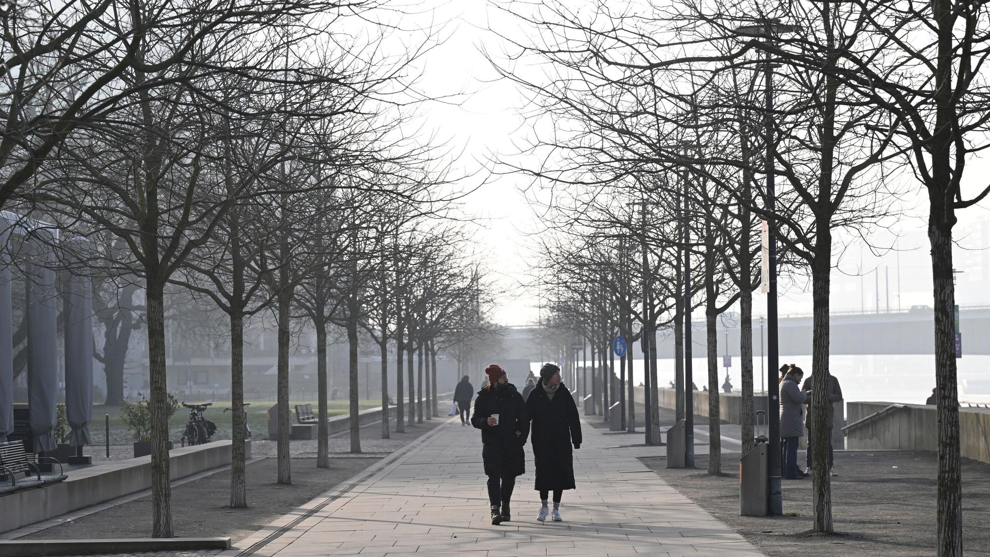 19.01.2025, Nordrhein-Westfalen, Köln: Spaziergänger gehen im diesigen Wetter am Rheinufer. Foto: Roberto Pfeil/dpa +++ dpa-Bildfunk +++