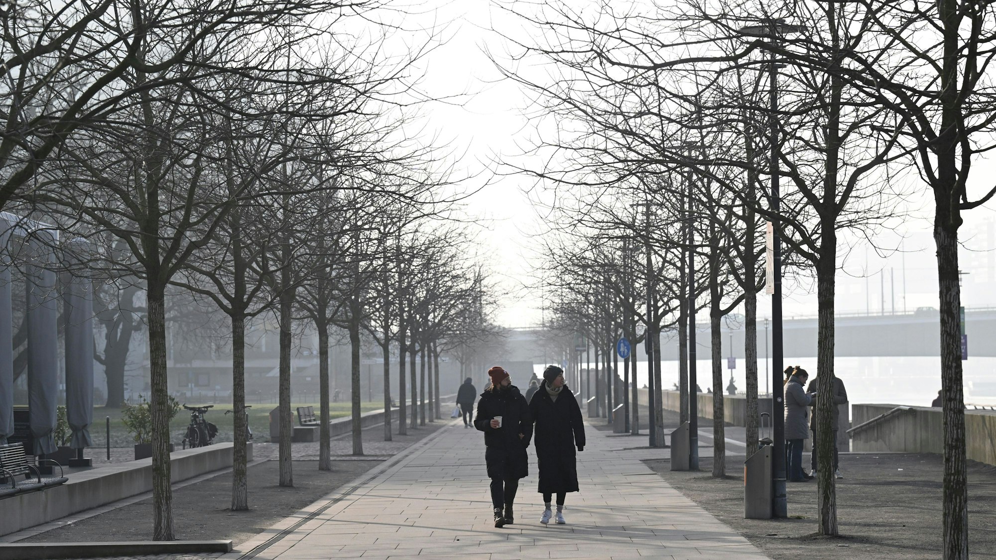 19.01.2025, Nordrhein-Westfalen, Köln: Spaziergänger gehen im diesigen Wetter am Rheinufer. Foto: Roberto Pfeil/dpa +++ dpa-Bildfunk +++