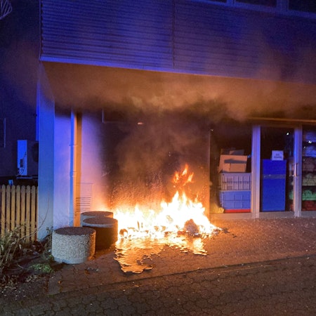 Vor einem Haus brennt eine Mülltonne.