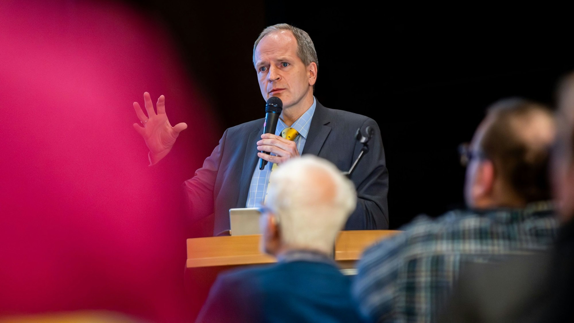 Das Bild zeigt Ingo Hessenius mit einem Mikrofon in der linken Hand an einem Rednerpult.