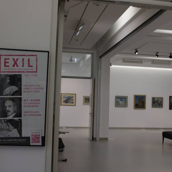 Ein heller Ausstellungsraum, in dem einige gerahmte Gemälde hängen. Am Eingang hängt ein Plakat mit dem Titel „Exil -Die verschollene Generation 1933 - 1945“