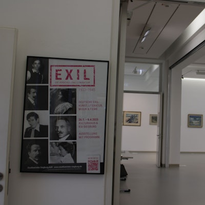 Ein heller Ausstellungsraum, in dem einige gerahmte Gemälde hängen. Am Eingang hängt ein Plakat mit dem Titel „Exil -Die verschollene Generation 1933 - 1945“
