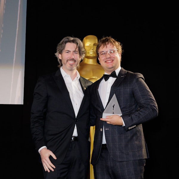 Zwei Männer vor einer großen Oscar-Statue.