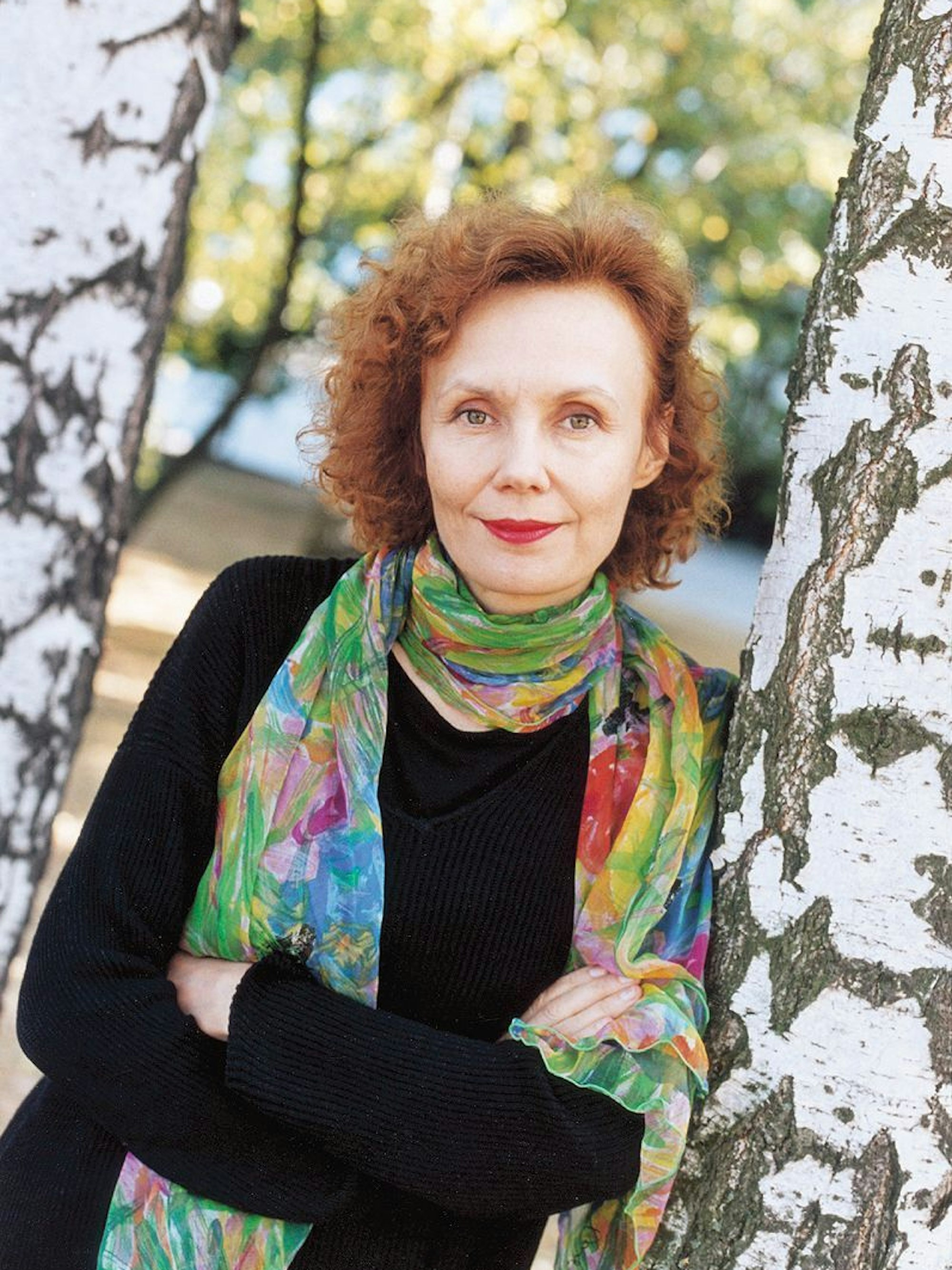 Kaija Saariaho lehnt mit verschränkten Armen an einem Baum.