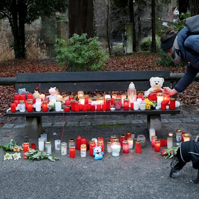 Eine Frau stellt eine Trauerkerze neben Blumen und Kuscheltieren nach dem tödlichen Angriff in einem Park am Tatort auf einer Bank ab.