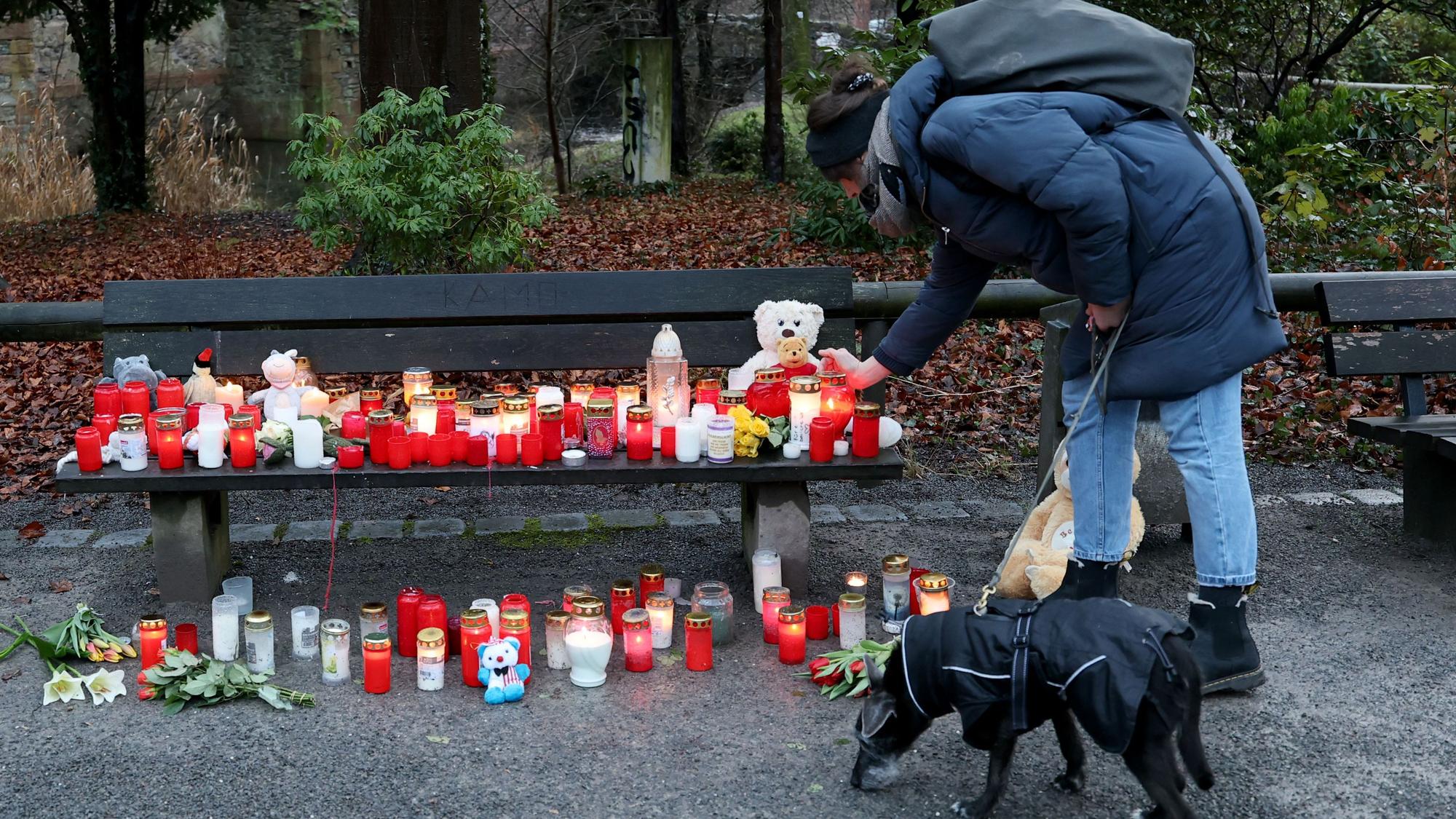 Eine Frau stellt eine Trauerkerze neben Blumen und Kuscheltieren nach dem tödlichen Angriff in einem Park am Tatort auf einer Bank ab.
